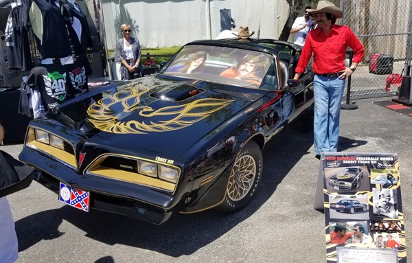 Burt Reynolds look-alike actor poses with fans next to the Bandit Trans Am